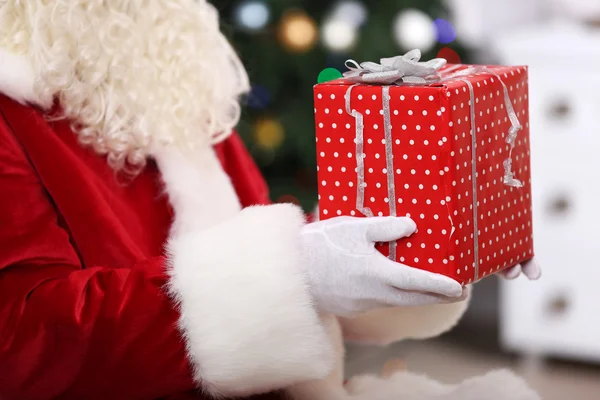 Santa dárek hospodářství na pozadí vánoční stromeček — Stock fotografie