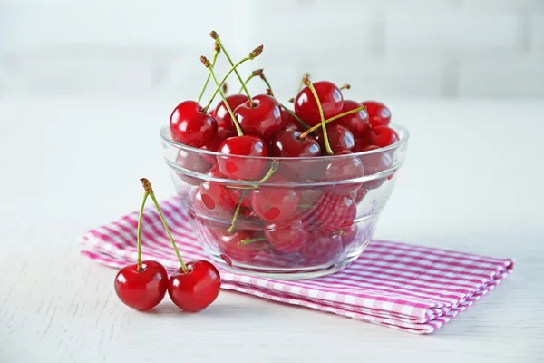 Körsbär i glasskål på bord, på ljus bakgrund — Stockfoto