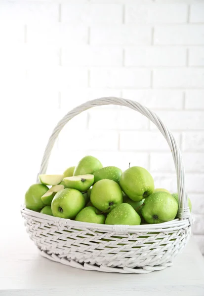 Gröna äpplen i rotting korg på vitt tegel vägg bakgrund — Stockfoto