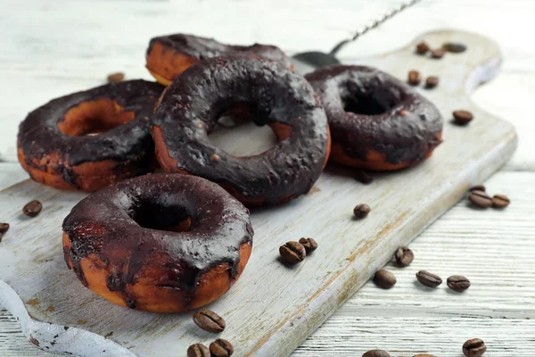 Delicious doughnuts with chocolate icing and coffee beans on table close up — Stock Photo, Image