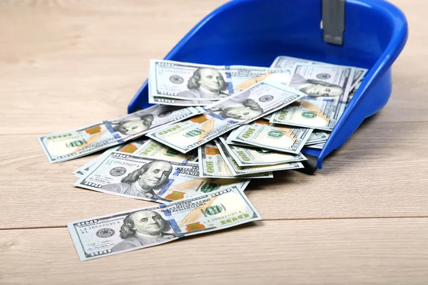 Dollars in garbage scoop on wooden floor background — Stock Photo, Image