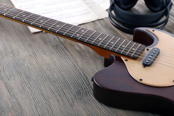 Elektrická kytara s sluchátka a hudebniny na dřevěný stůl zblízka — Stock fotografie