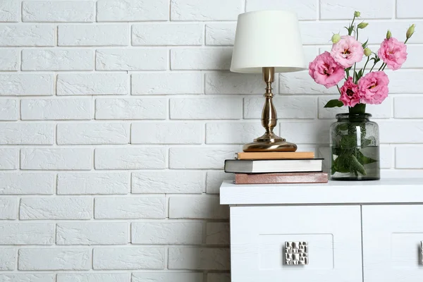 Hermosas flores con lámpara de mesa sobre fondo de pared de ladrillo — Foto de Stock