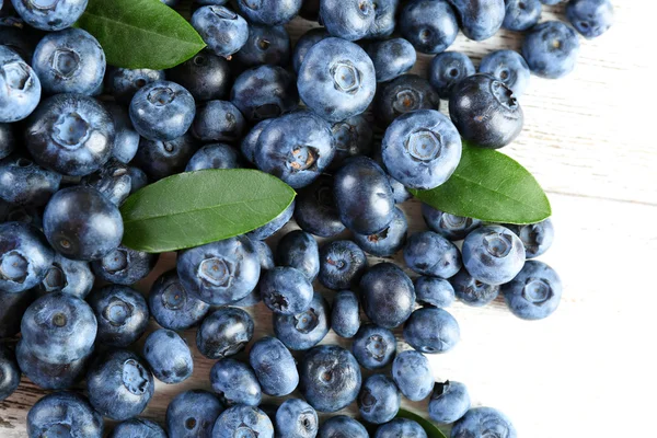 Leckere reife Blaubeeren mit grünen Blättern auf Holztisch aus nächster Nähe — Stockfoto