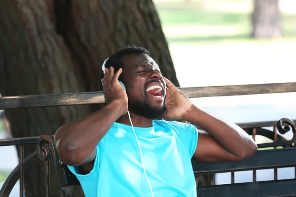 African American man with headphones on bench in park — Stock Photo, Image