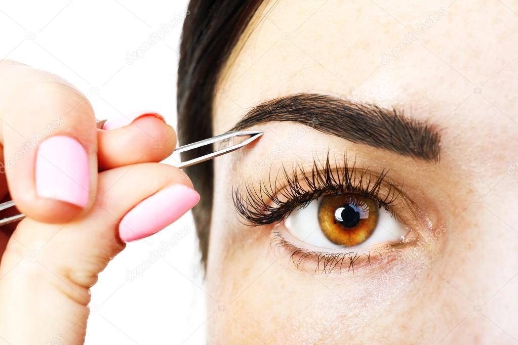 Young woman plucking eyebrows with tweezers close up