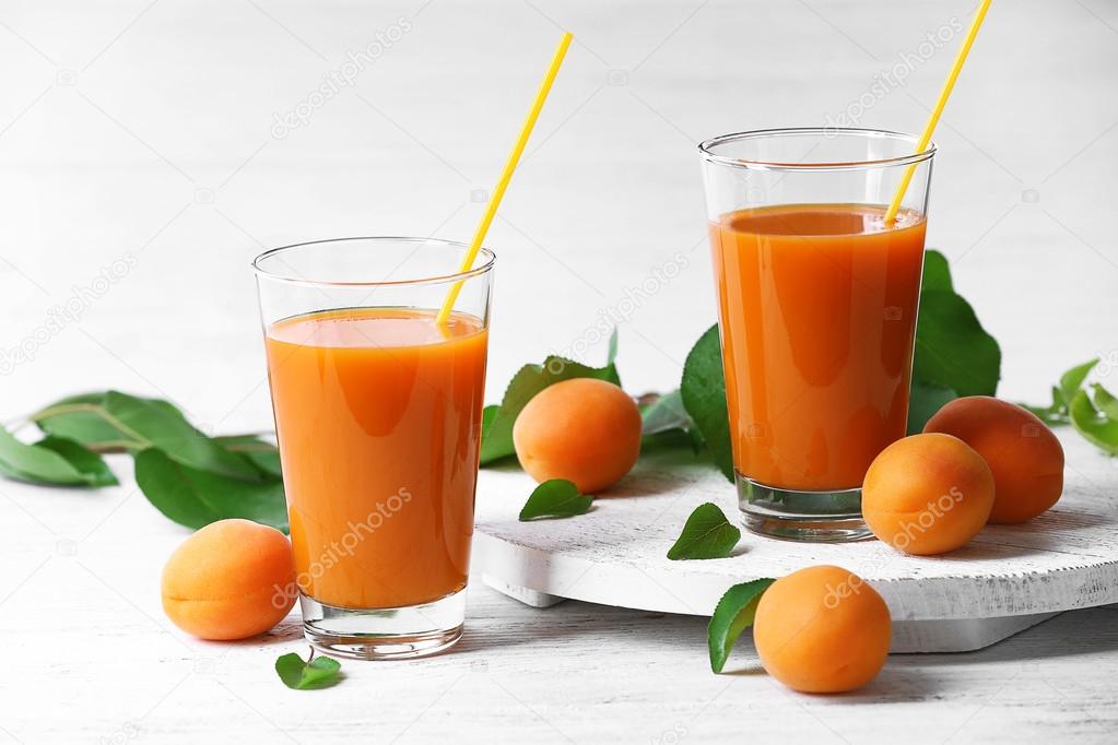 Glasses of apricots juice on wooden table on white background