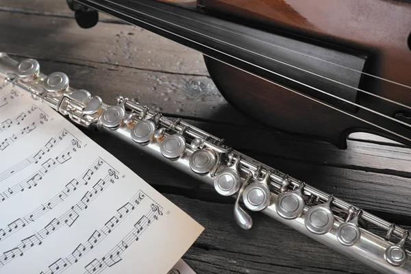 Flöjt och violin med noter på träbord nära håll — Stockfoto