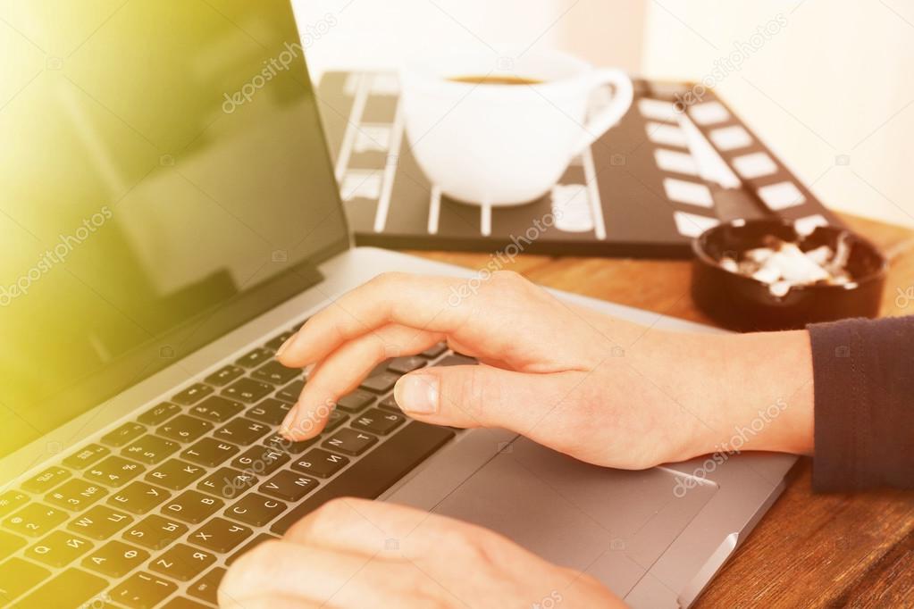 Female hands of scriptwriter working on laptop at desk on cupboard background