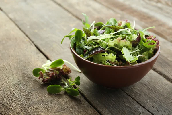 Fresh mixed green salad in bowl on wooden table close up — Stock Photo, Image
