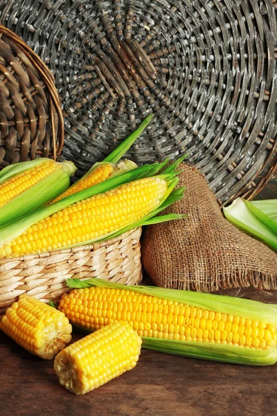 Fresh corn on cobs in wicker basket on wooden table, closeup — Stock Photo, Image