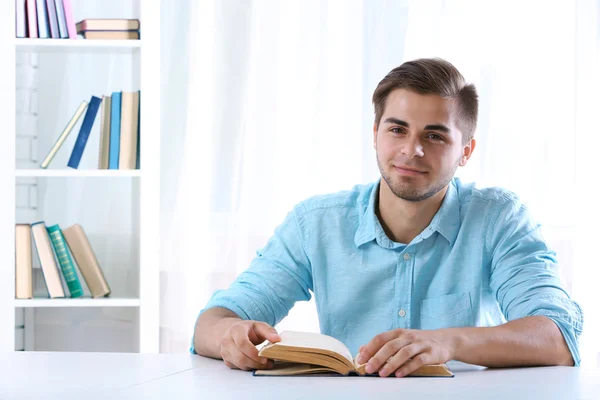 Молодий чоловік читає книгу за столом у кімнаті — стокове фото