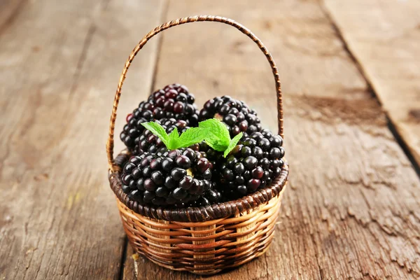 Reife Brombeeren mit grünen Blättern im Weidenkorb auf hölzernem Hintergrund — Stockfoto