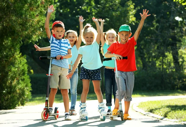 Crianças andando em scooters e patins no parque — Fotografia de Stock