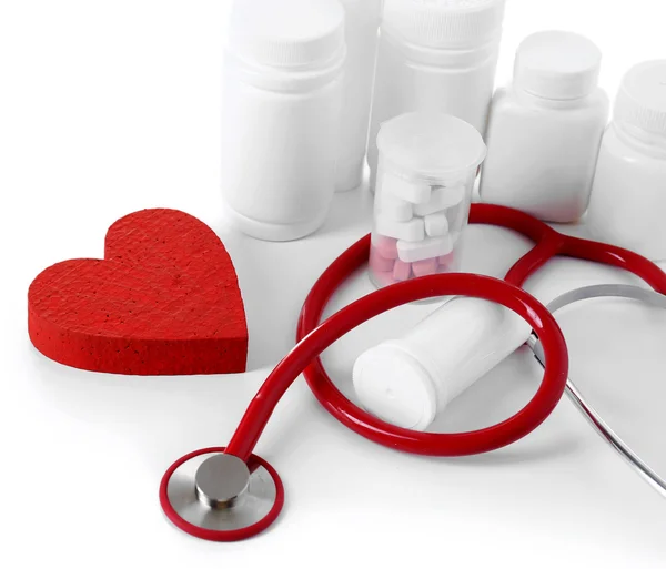 Stéthoscope médical avec bouteilles de pilules et coeur rouge isolé sur blanc — Photo