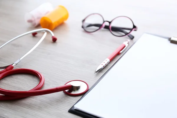 Medical stethoscope with clipboard and pills on wooden table close up — Stock Photo, Image