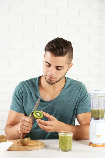 Jovem homem descascando kiwi, preparando suco de laranja — Fotografia de Stock