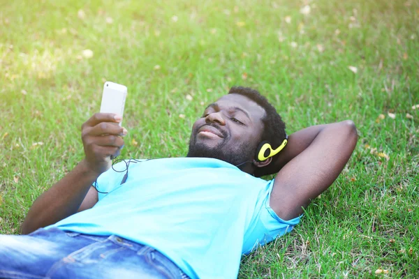 アフリカ系アメリカ人男は公園で緑の草の上にヘッドフォンで音楽を聴く — ストック写真