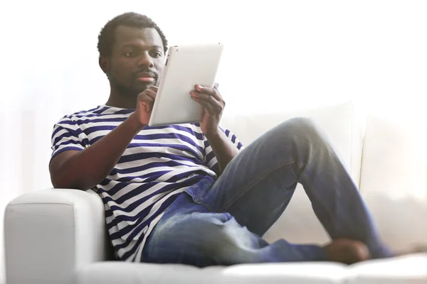 Hombre afroamericano con tablet y tarjeta de crédito en sofá en la habitación —  Fotos de Stock