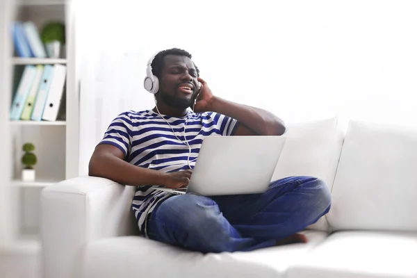 Афроамериканец слушает музыку с наушниками на диване в номере — стоковое фото