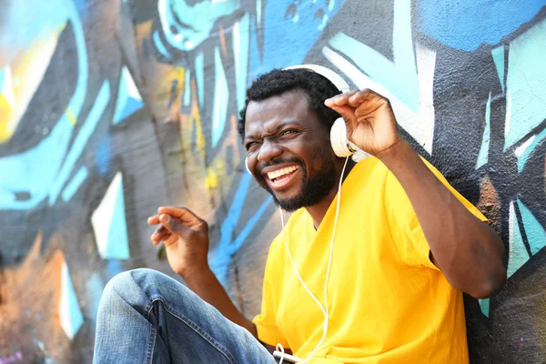 African American man with headphones on graffiti wall background — Stock Photo, Image