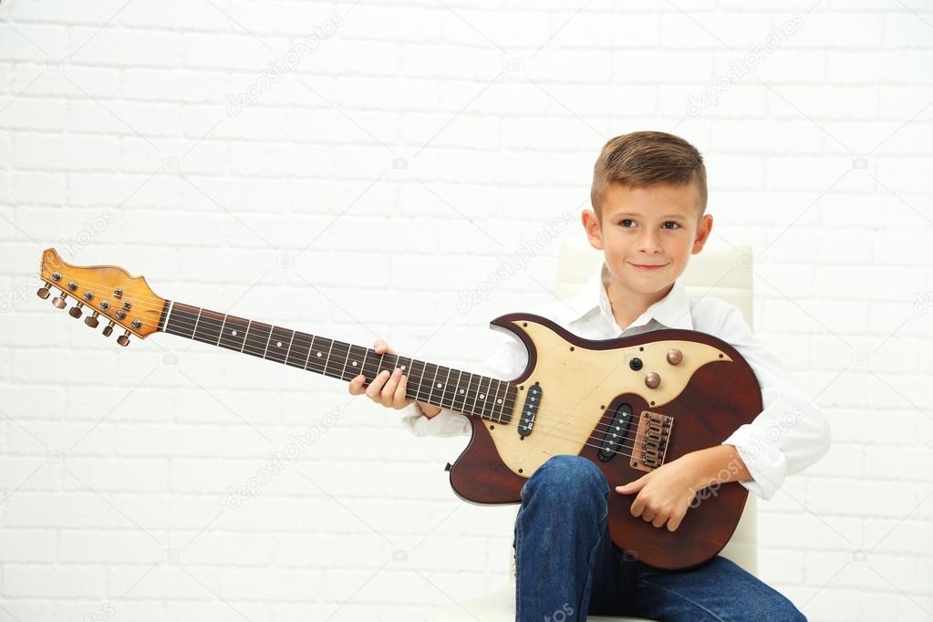 Little boy playing guitar on light background