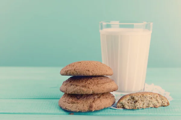 Leckere Kekse und ein Glas Milch auf dem Tisch vor türkisfarbenem Hintergrund — Stockfoto