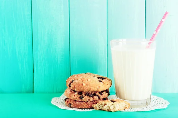 Biscoitos saborosos e copo de leite na mesa em fundo turquesa — Fotografia de Stock