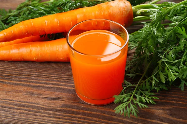 Glas morotsjuice med grönsaker på träbord nära håll — Stockfoto