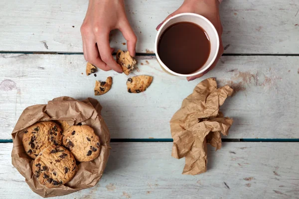 Frauenhände halten Tasse Kaffee und Kekse auf Holztisch in Großaufnahme — Stockfoto