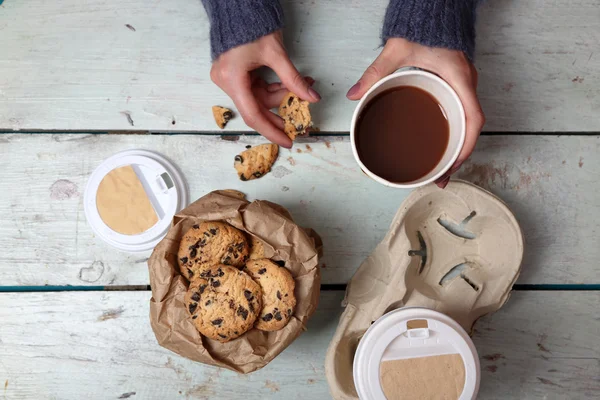 Female hands holding cup of coffee and cookies on wooden table close up — Stock Photo, Image