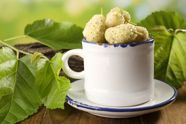 Mûres mûres mûres dans une tasse avec des feuilles vertes sur la table fermer — Photo