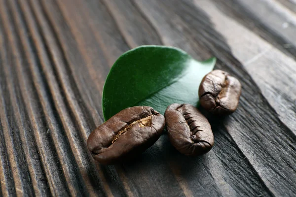 Grãos de café com folha sobre fundo de madeira — Fotografia de Stock