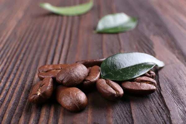Kaffebönor med blad på trä bakgrund — Stockfoto