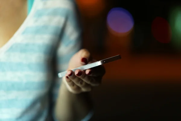 Female hand with mobile phone on blurred night lights background — Stock Photo, Image