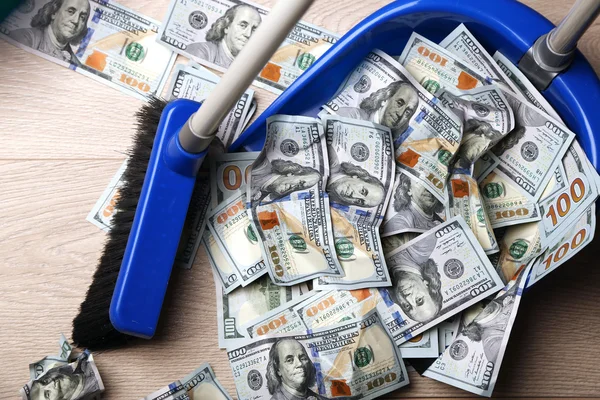 Broom sweeps dollars in garbage scoop on wooden floor background — Stock Photo, Image