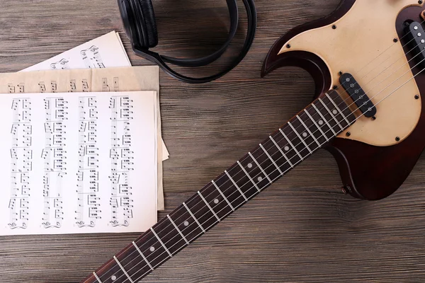 Electric guitar with headphones and music notes on wooden table close up