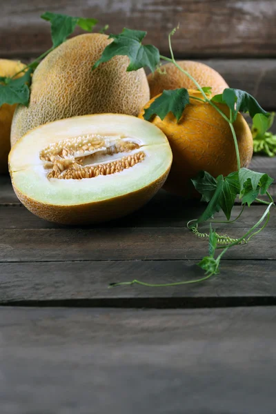 Meloni maturi con foglie verdi su sfondo di legno — Foto Stock