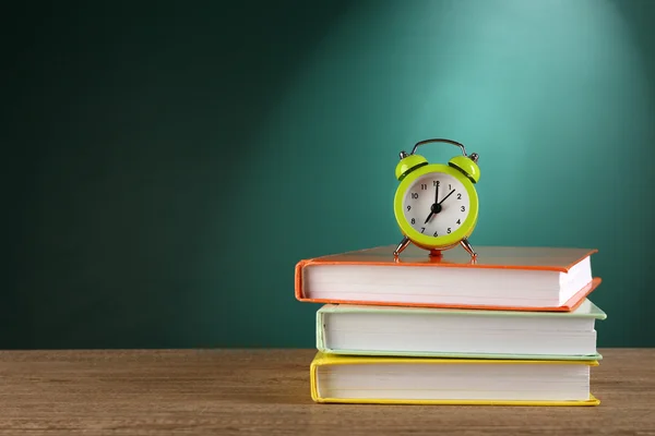 Masa üzerinde yeşil kara tahta arka plan ile çalar saat kitap yığını — Stok fotoğraf