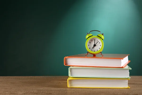 Montón de libros con despertador en escritorio sobre fondo de pizarra verde —  Fotos de Stock