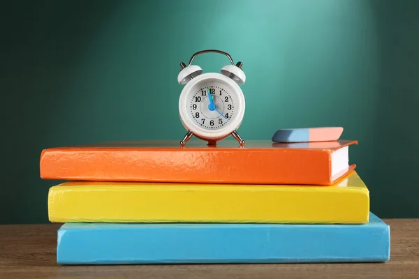 Stack of books with alarm clock and eraser on green chalkboard background — Stock Photo, Image