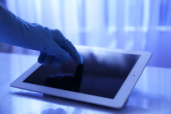 Main de médecin en gant de caoutchouc à l'aide d'une tablette au bureau — Photo