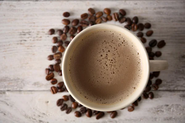 Cup of coffee with beans on wooden table, top view — Stock Photo, Image