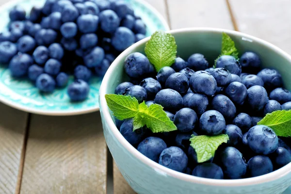 Cup and plate with fresh blueberries on wooden table close up — Stock Photo, Image