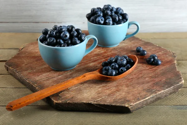 Fresh blueberries in cups and spoon on wooden table close up — Stock Photo, Image