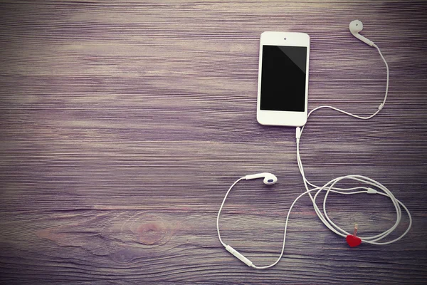 Mobiele telefoon en koptelefoon met rood hart op houten achtergrond — Stockfoto