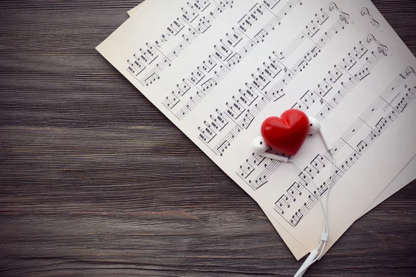 Fones de ouvido com coração vermelho e notas de música em fundo de madeira — Fotografia de Stock