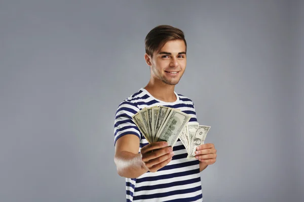 Pohledný mladý muž drží peníze na šedém pozadí — Stock fotografie
