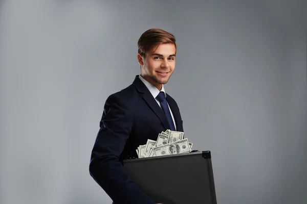 Homem elegante segurando caso com dinheiro em fundo cinza — Fotografia de Stock