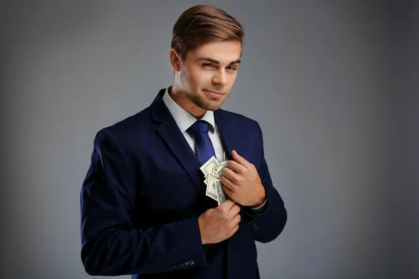 Homem elegante em terno segurando dinheiro em fundo cinza — Fotografia de Stock